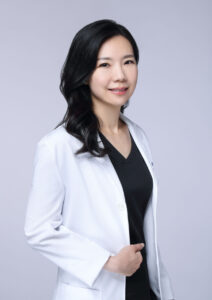 Professional woman in a white blazer smiles confidently against a plain background.